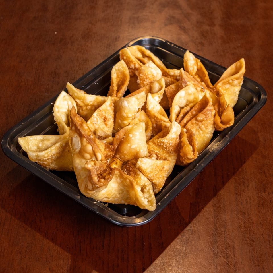 A black rectangular container filled with golden-brown fried wontons, resting on a dark wooden table.