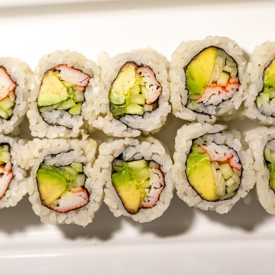 Two rows of California sushi rolls with avocado, cucumber, and crab meat on a white plate.