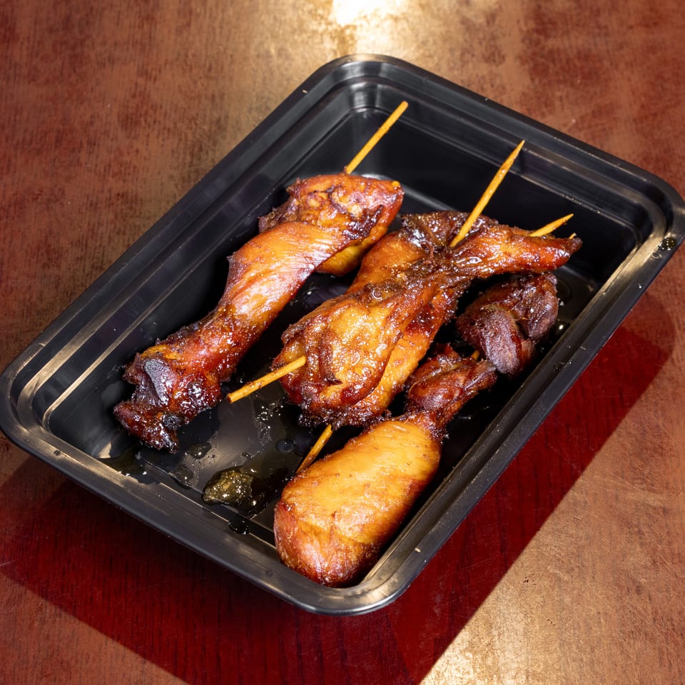 Sweet and sticky chicken wings and drumettes on skewers in a black takeout container.