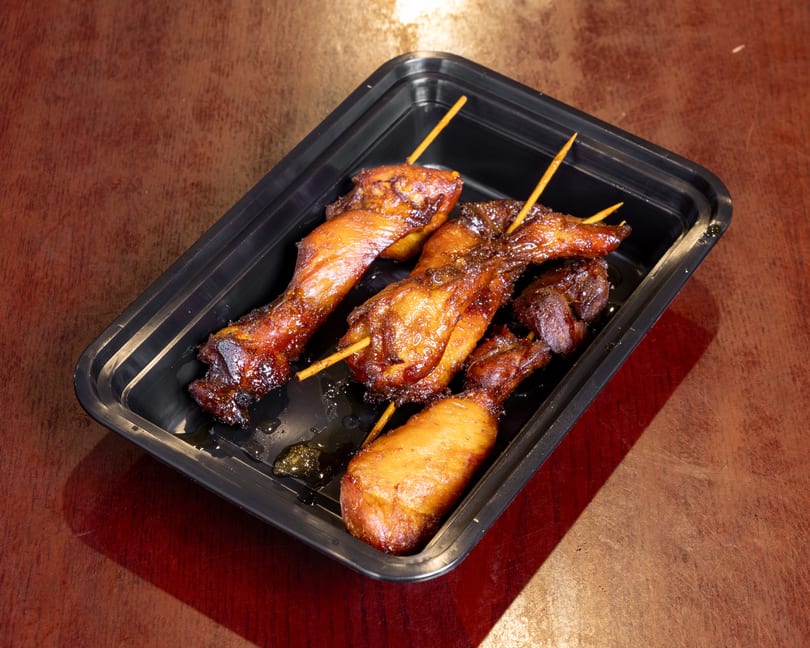 Sweet and sticky chicken wings and drumettes on skewers in a black takeout container.