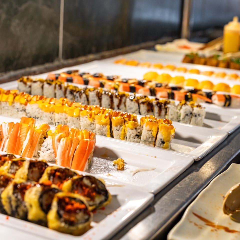 A sushi buffet line with various rolls, including crab, spicy tuna, and fried options.