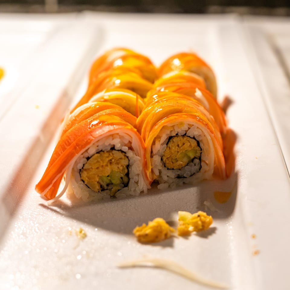 Rows of sushi rolls with crab stick and mango topping on a white serving dish.