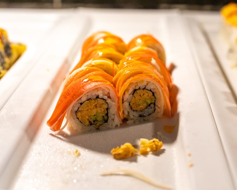 Rows of sushi rolls with crab stick and mango topping on a white serving dish.