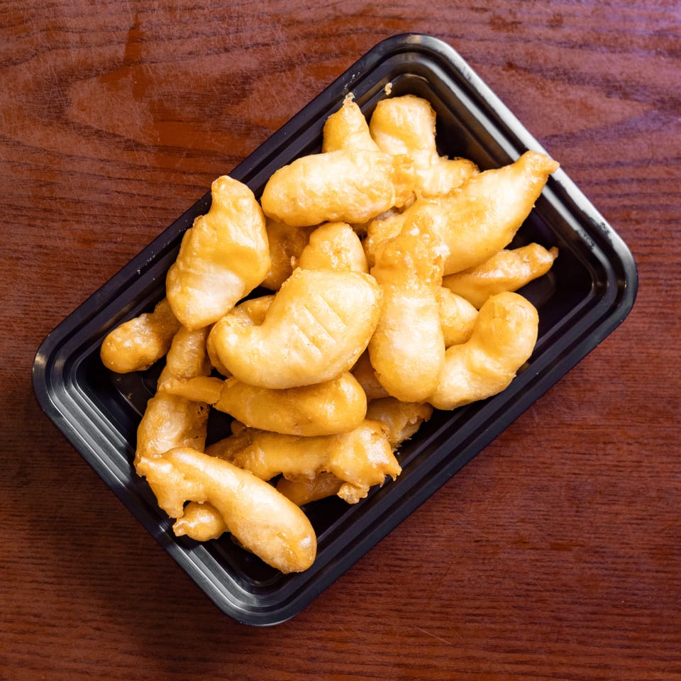 Golden-brown fried chicken pieces in a black takeout container on a wooden table.