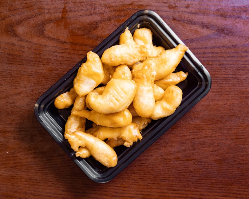 Golden-brown fried chicken pieces in a black takeout container on a wooden table.