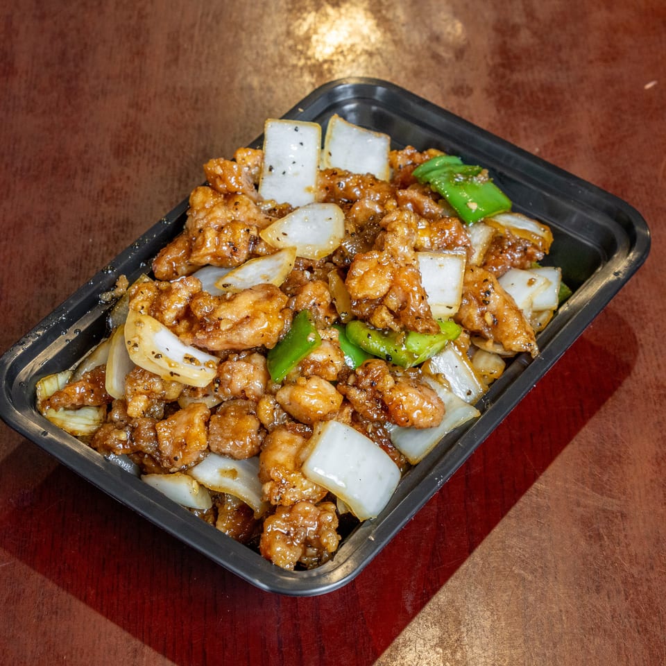 Black pepper chicken with onions and green peppers in a black takeout container.