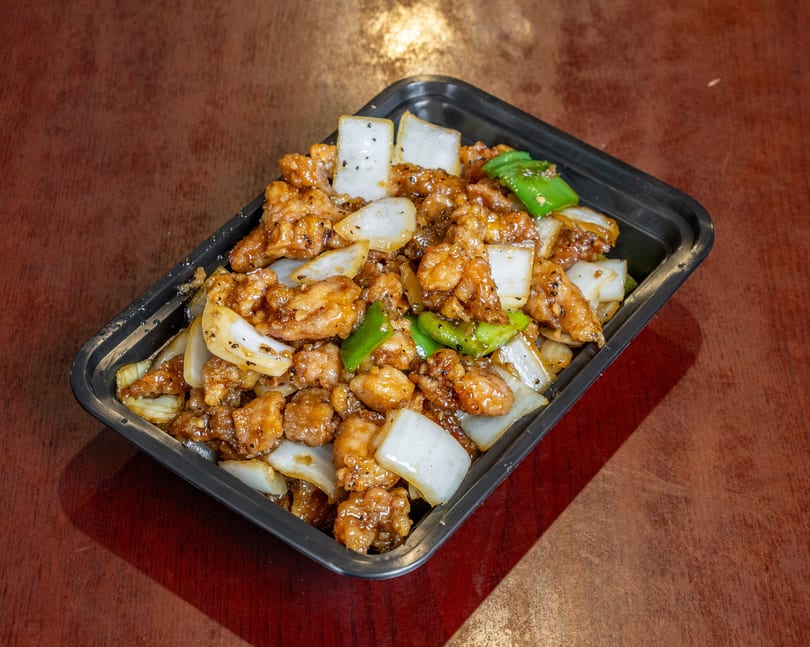 Black pepper chicken with onions and green peppers in a black takeout container.