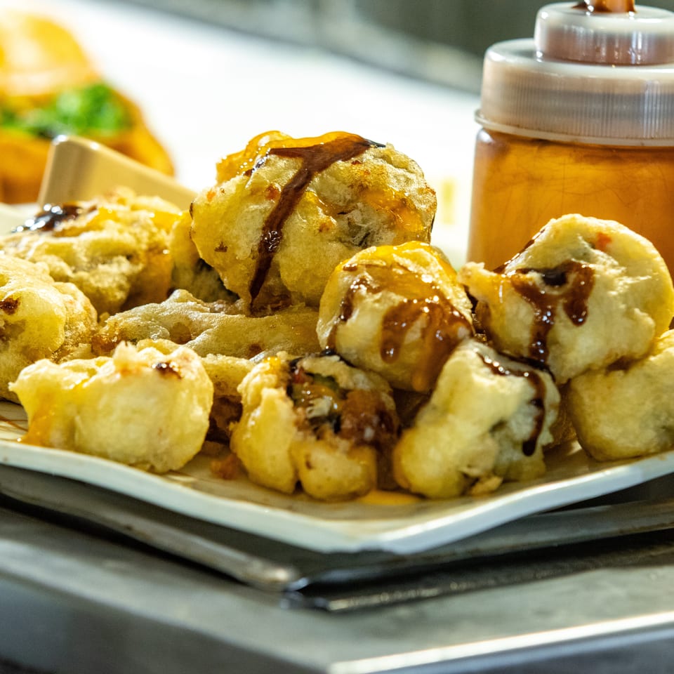 Fried tempura-style sushi rolls drizzled with dark sauce and honey on a white plate.