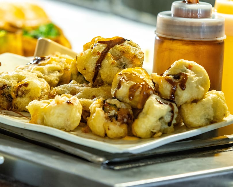 Fried tempura-style sushi rolls drizzled with dark sauce and honey on a white plate.