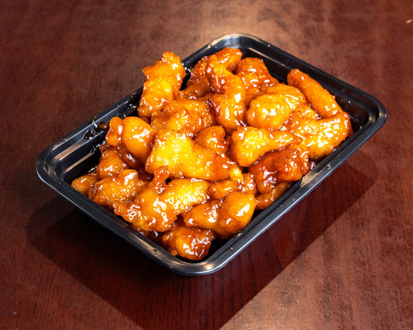 Orange chicken in a black takeout container on a dark wooden table.