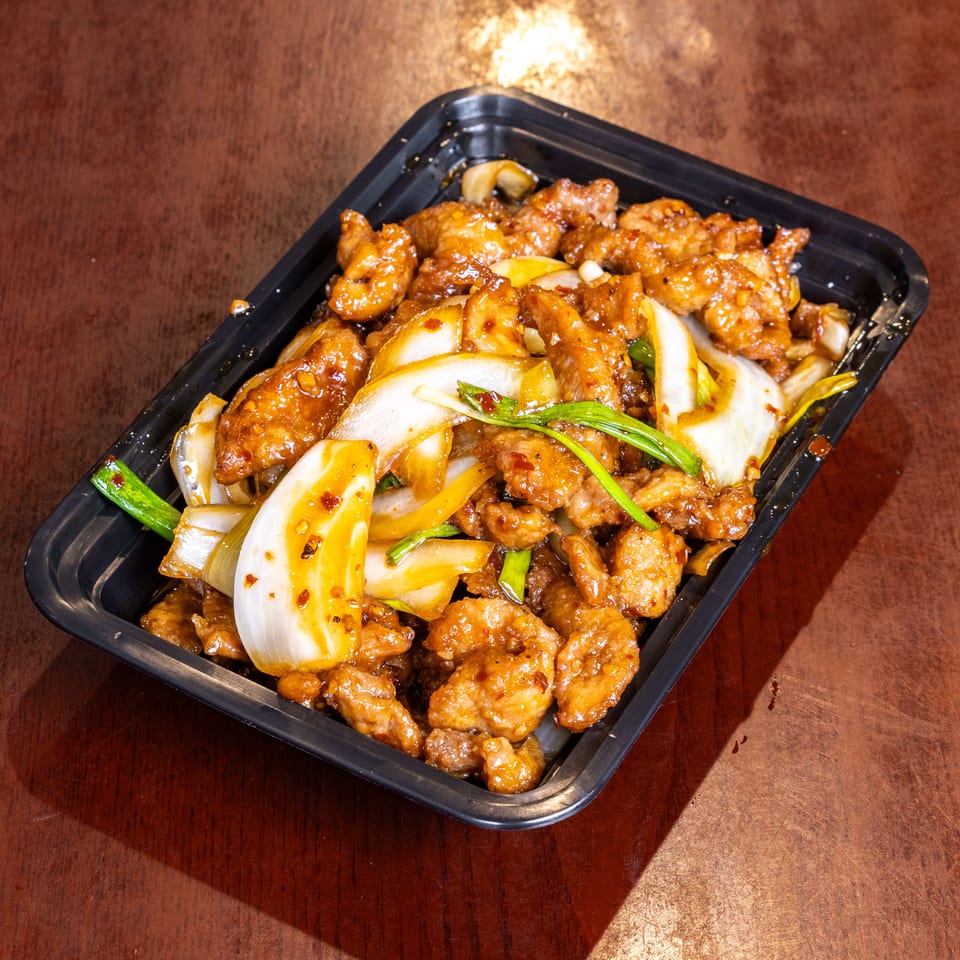 Sweet and sour chicken with onions and green onions in a black takeout container.