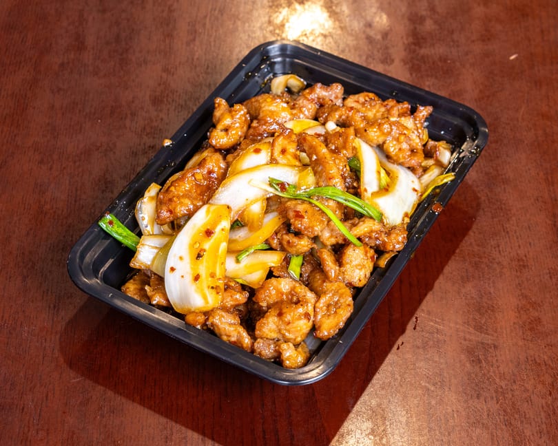 Sweet and sour chicken with onions and green onions in a black takeout container.